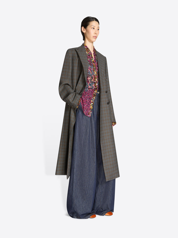 Person wearing a long gray coat and dark jeans on a white background