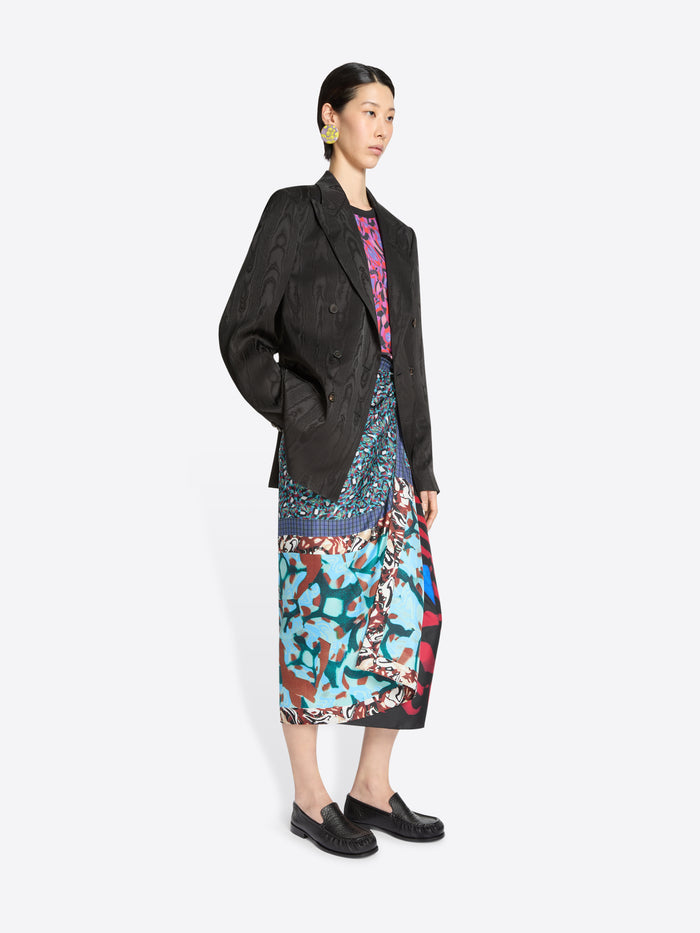 Woman wearing a dark brown blazer with a colorful skirt on a white background