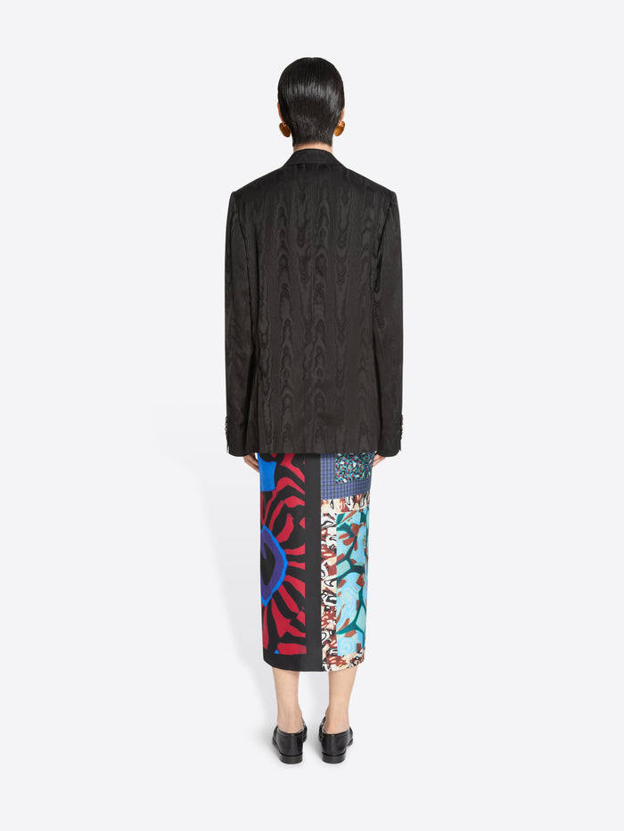 Back view of a person wearing a dark brown blazer and colorful patterned skirt on a white background
