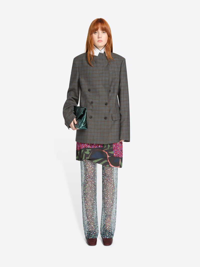 Person wearing a gray checkered blazer with colorful skirt and pants on a white background