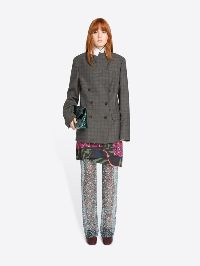 Person wearing a gray checkered blazer with colorful skirt and pants on a white background