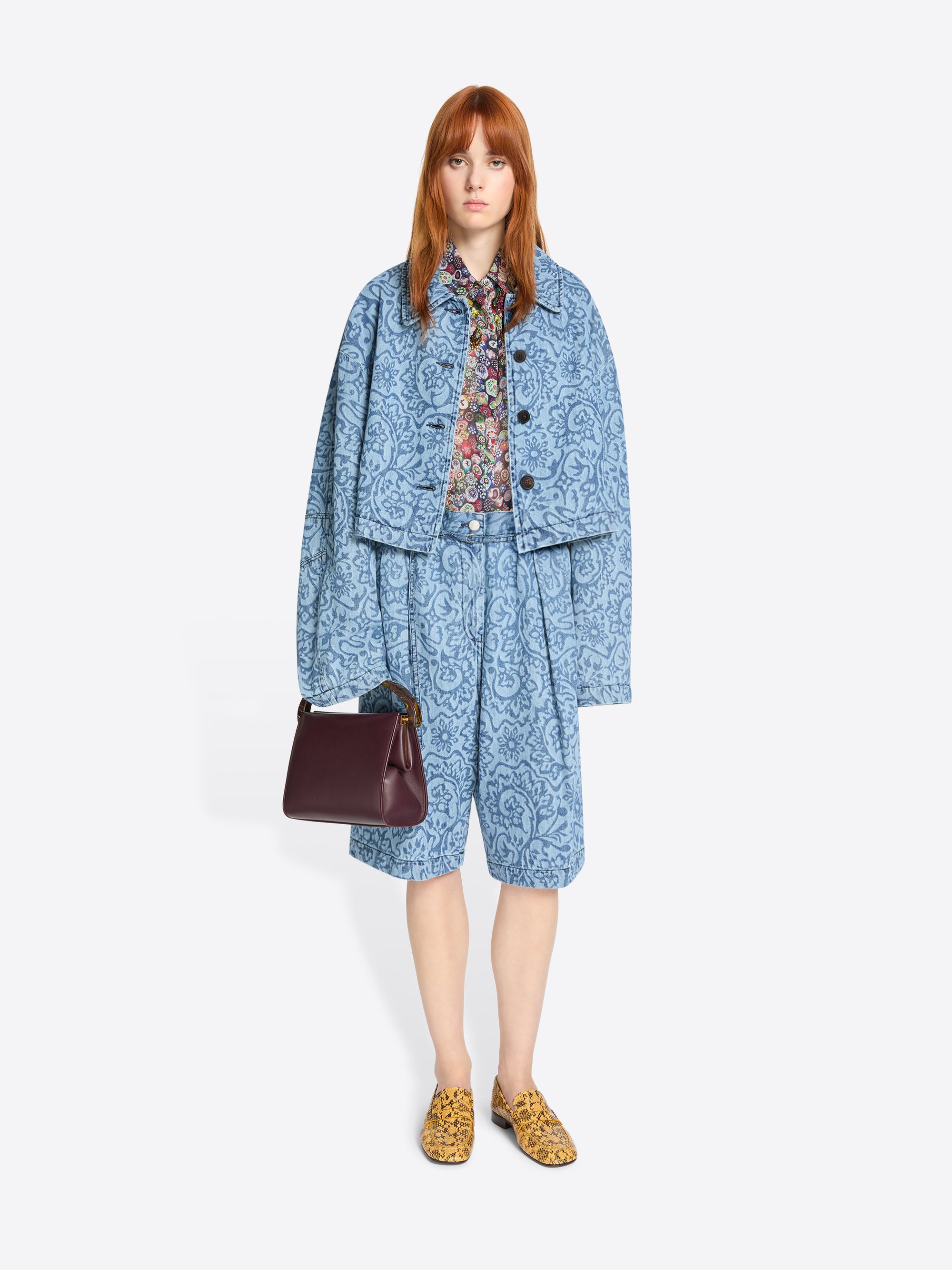 Woman wearing a blue patterned outfit with a brown handbag on a white background