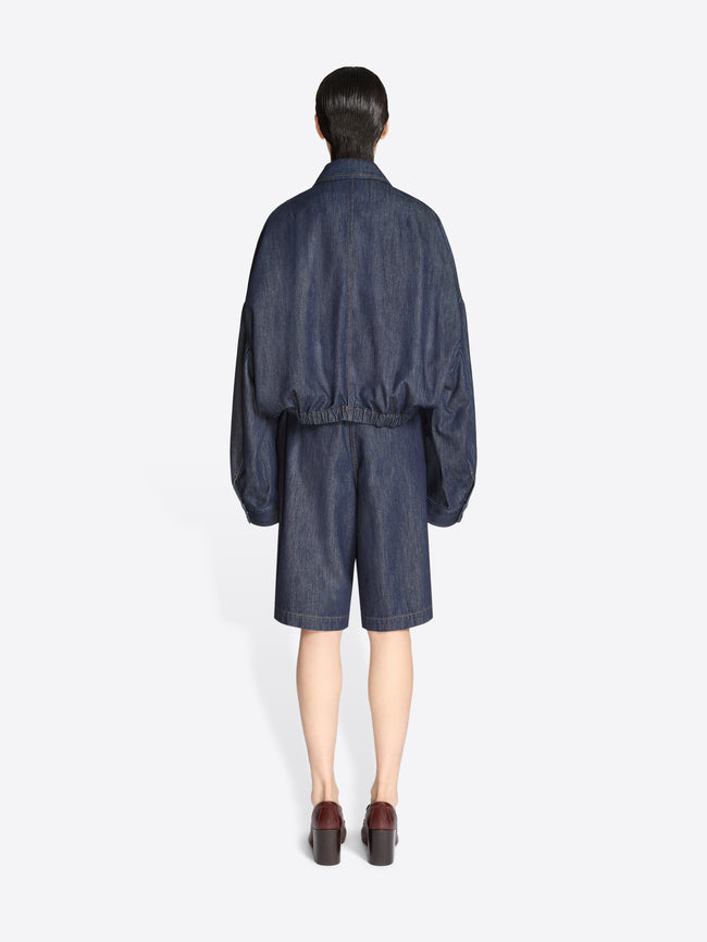 Back view of a person wearing a dark denim outfit on a white background