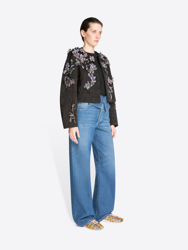 Woman wearing a black floral jacket and blue jeans on a white background