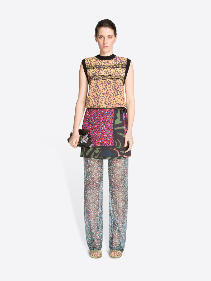 Model wearing a colorful outfit with a patterned top, skirt and pants on a white background
