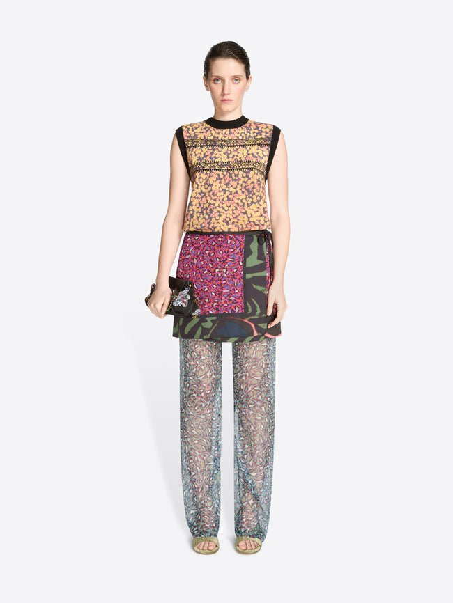 Model wearing a colorful outfit with a patterned top, skirt and pants on a white background