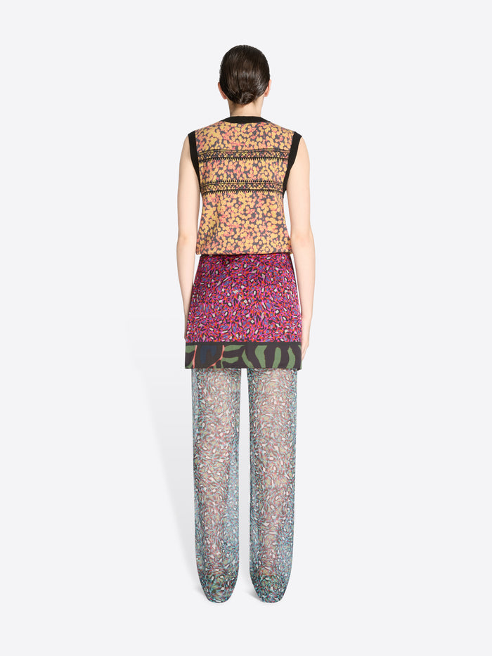 Back view of a person wearing a patterned top, skirt and pants on a white background