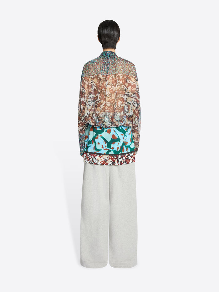 Back view of a person wearing a patterned blouse and light-colored pants on a white background
