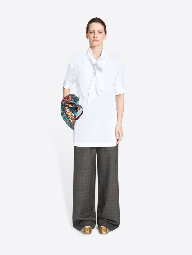 Person wearing a white shirt and gray checkered pants holding a colorful bag on a white background