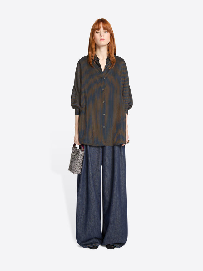 Woman wearing a dark brown oversized shirt and wide-leg denim pants on a white background