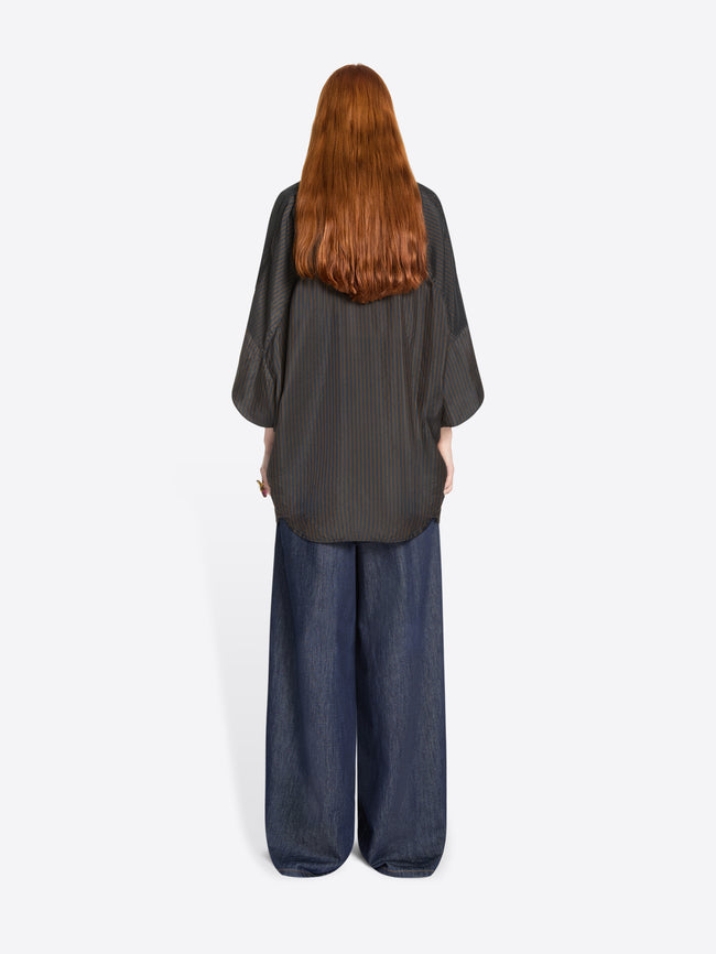 Back view of a person wearing a dark gray shirt and blue denim pants on a white background