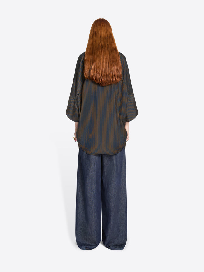 Back view of a person wearing a dark gray shirt and blue denim pants on a white background