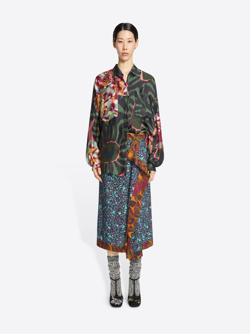 Model wearing a colorful floral shirt and long patterned skirt on a white background