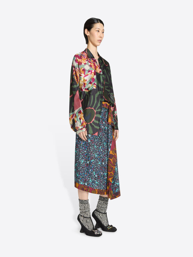 Woman wearing a long, patterned skirt and patterned shirt on a white background