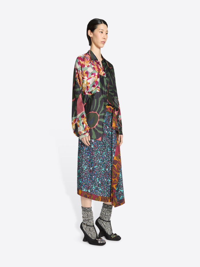 Woman wearing a long, patterned skirt and patterned shirt on a white background