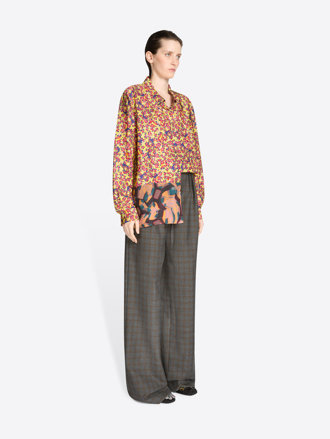 Person wearing a colorful patterned blouse and gray checkered pants on a white background