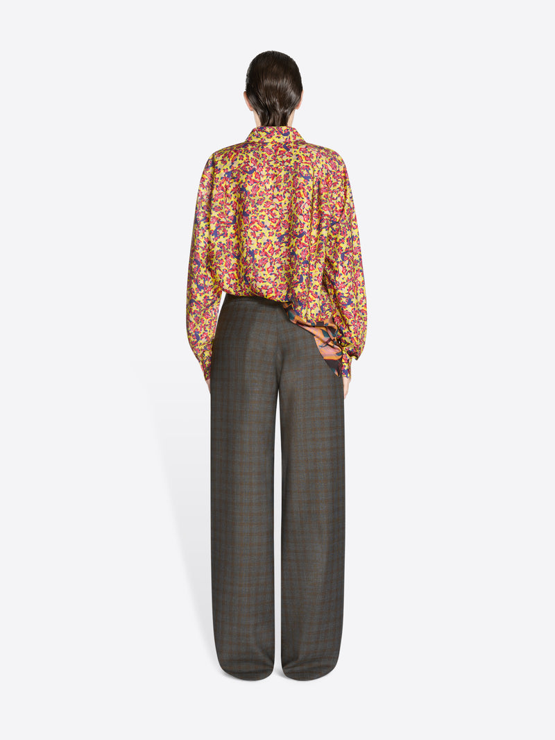 Back view of a person wearing a colorful floral blouse and gray checkered pants on a white background