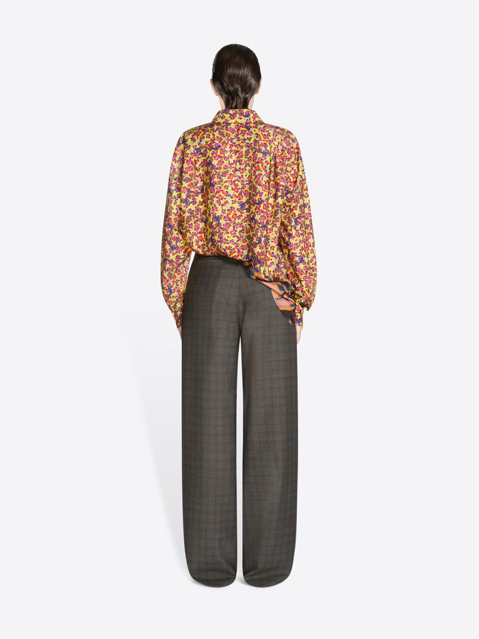 Back view of a person wearing a colorful floral blouse and gray checkered pants on a white background