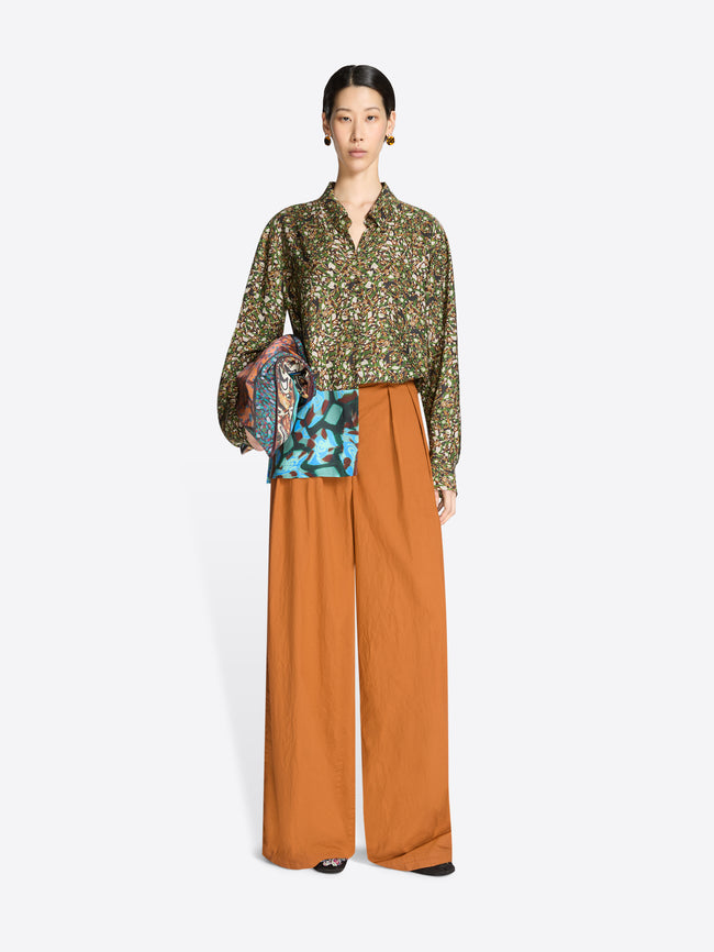 Model wearing a floral blouse and wide-leg orange pants with a white background