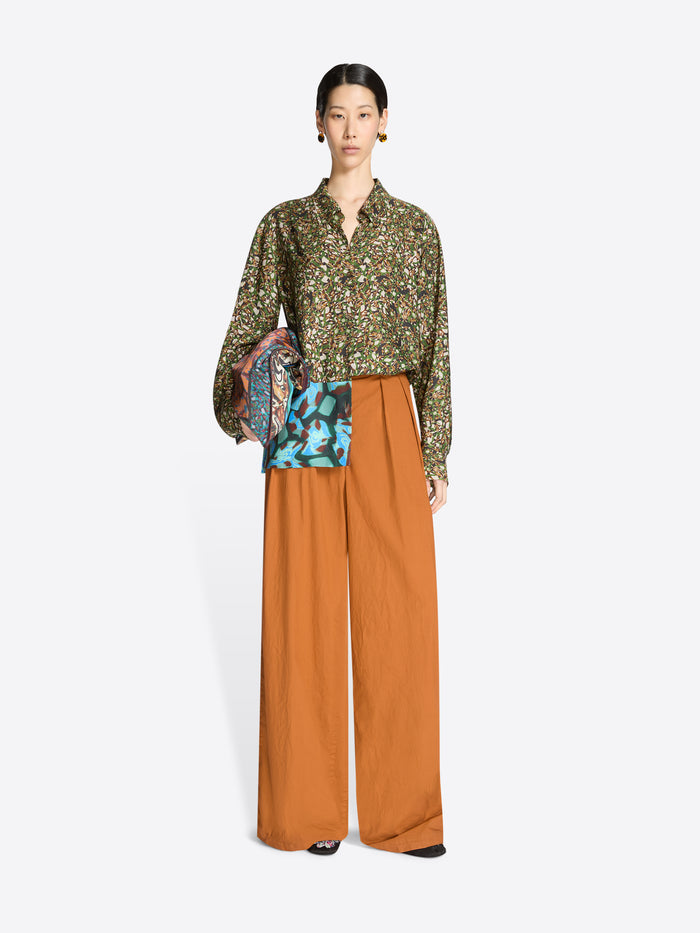 Model wearing a floral blouse and wide-leg orange pants with a white background