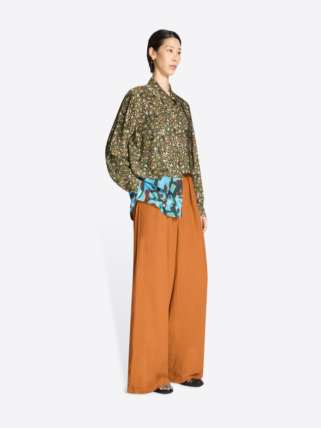 Woman wearing a patterned blouse and wide-leg orange pants on a white background