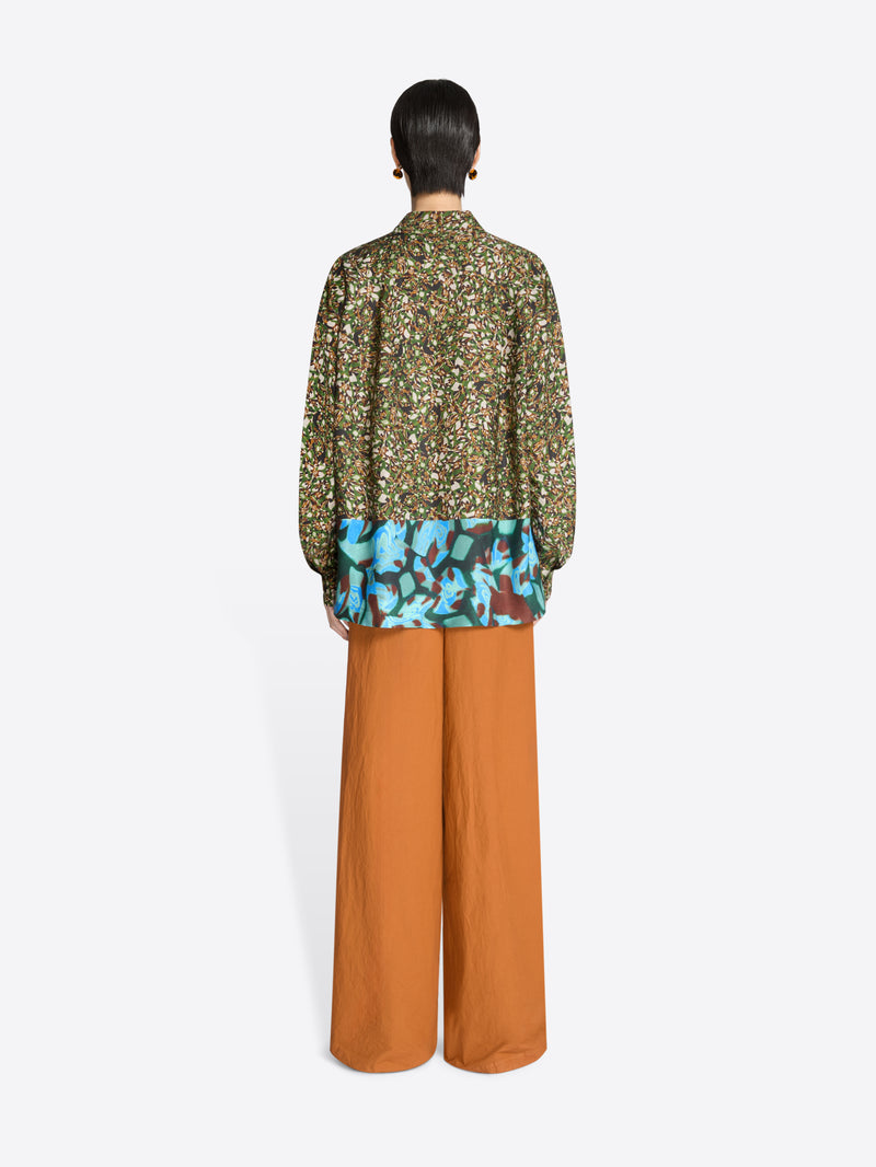Back view of a person wearing a floral blouse and orange pants on a white background