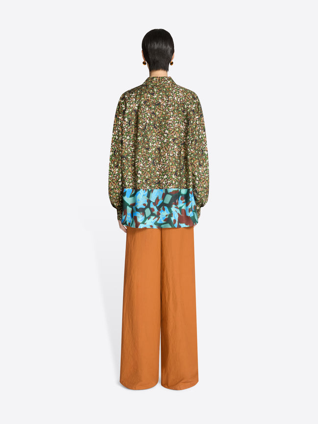 Back view of a person wearing a floral blouse and orange pants on a white background