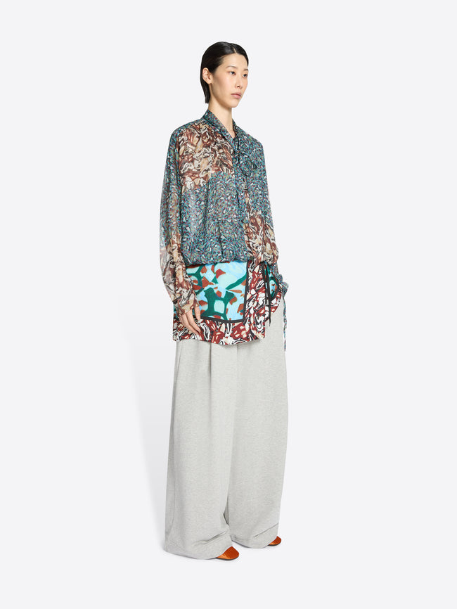 Woman wearing a patterned blouse and light-colored pants on a white background