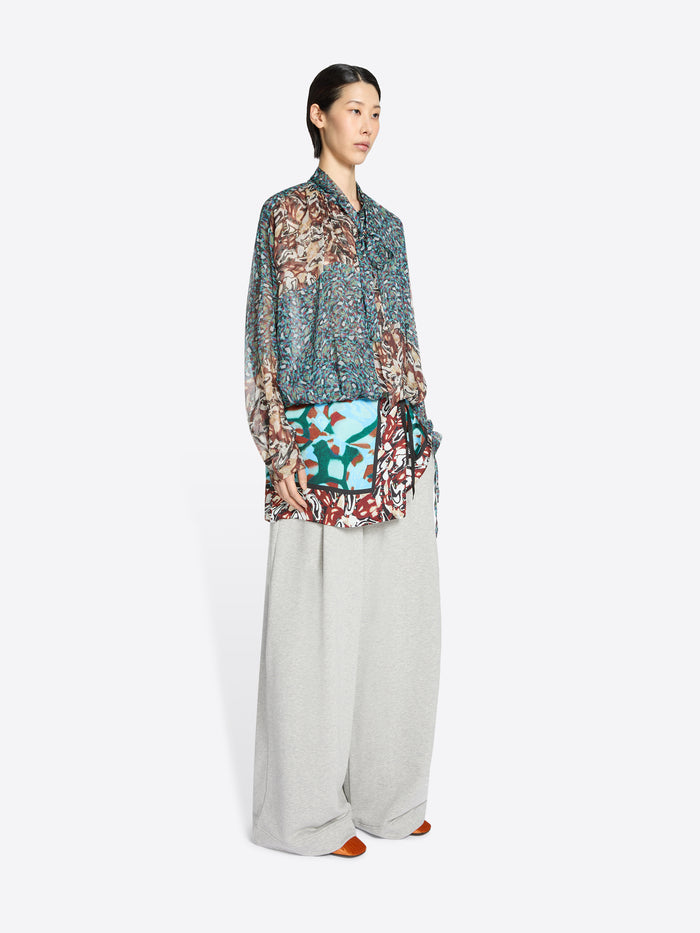 Woman wearing a patterned blouse and light-colored pants on a white background
