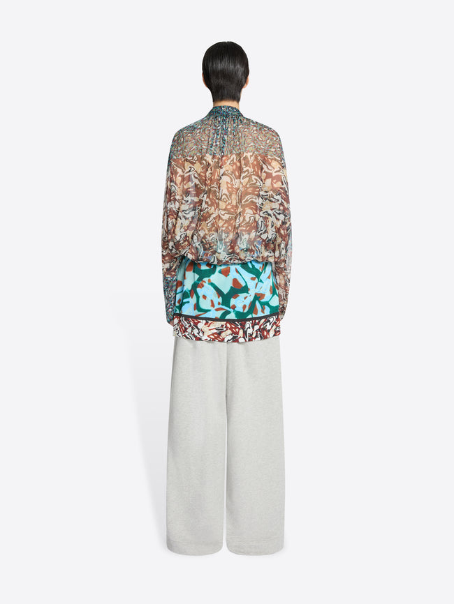 Back view of a person wearing a patterned blouse and light-colored pants on a white background