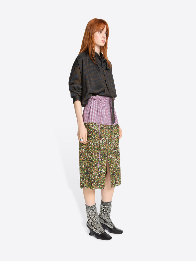 Woman wearing a brown shirt and green patterned skirt on a white background