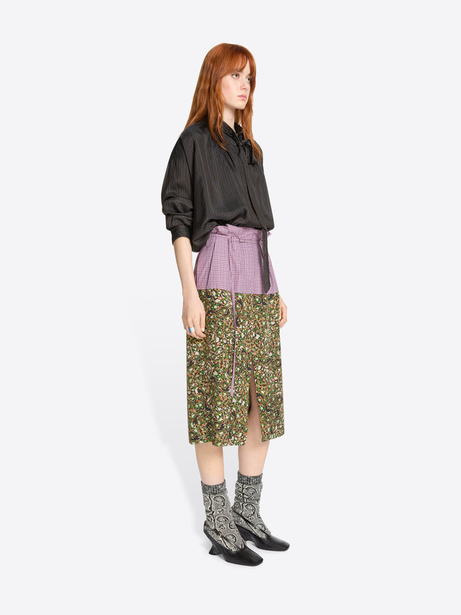 Woman wearing a brown shirt and green patterned skirt on a white background