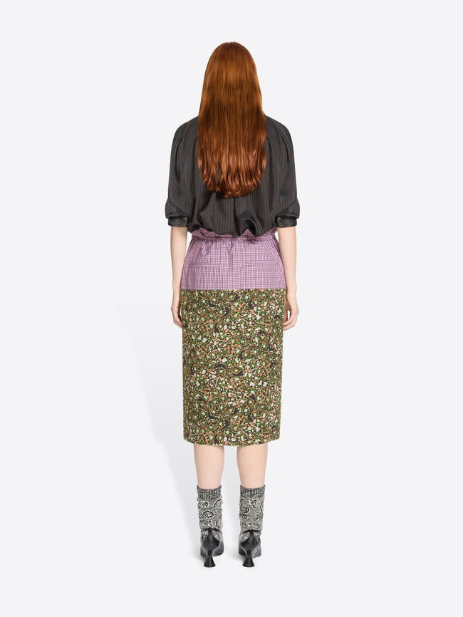 Back view of a person wearing a floral skirt and brown shirt on a white background