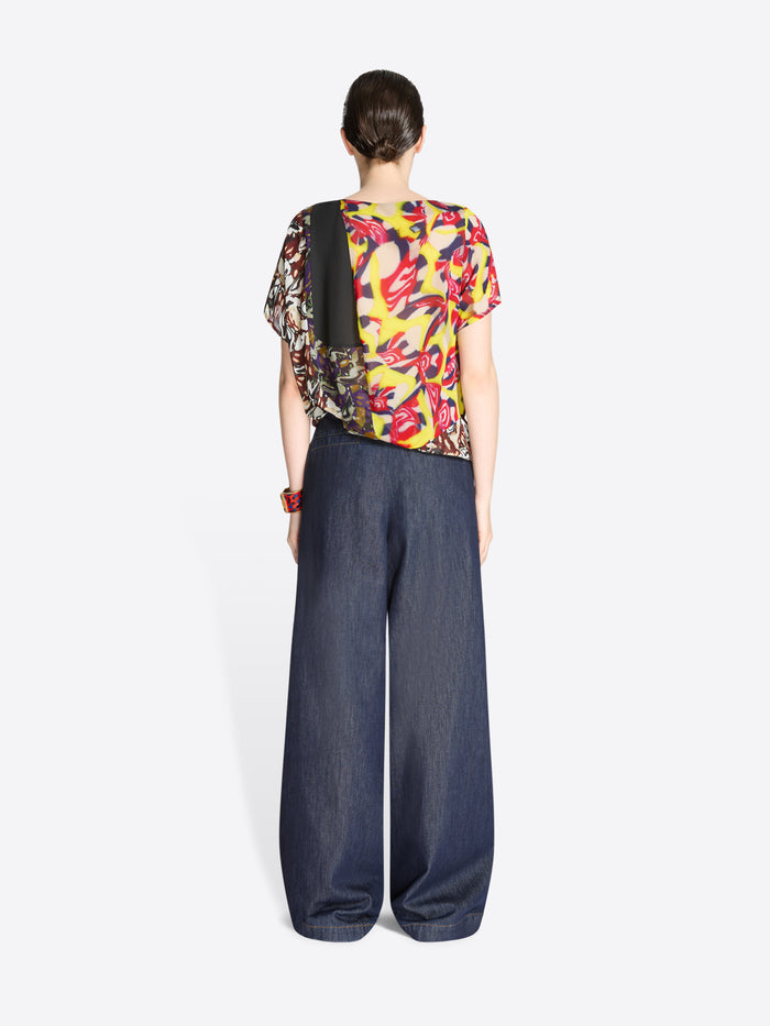 Person wearing a colorful top and dark blue denim pants on a white background