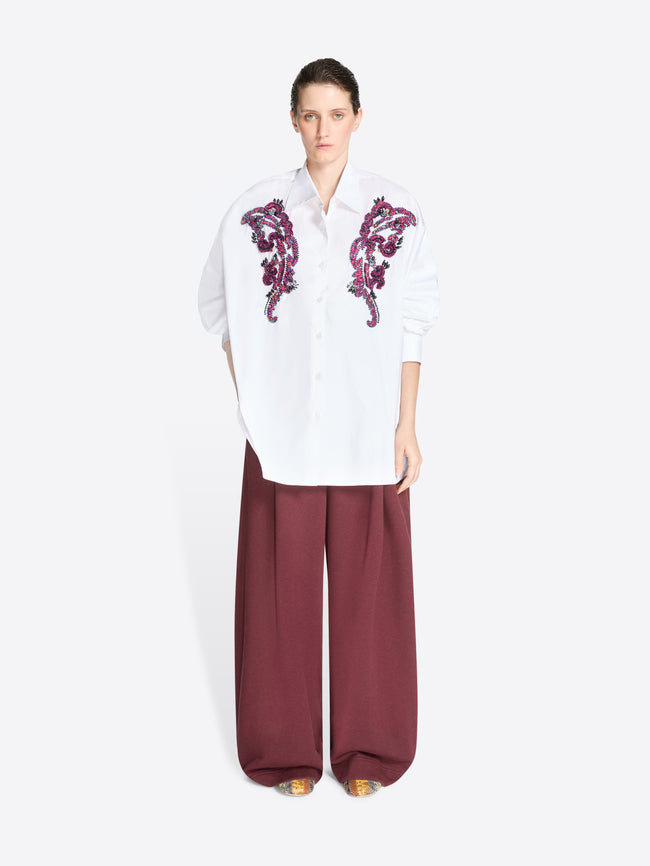 Woman wearing a white shirt with purple embroidery and burgundy pants on a white background