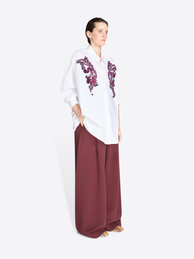 Woman wearing a white shirt with purple embroidery and burgundy pants on a white background