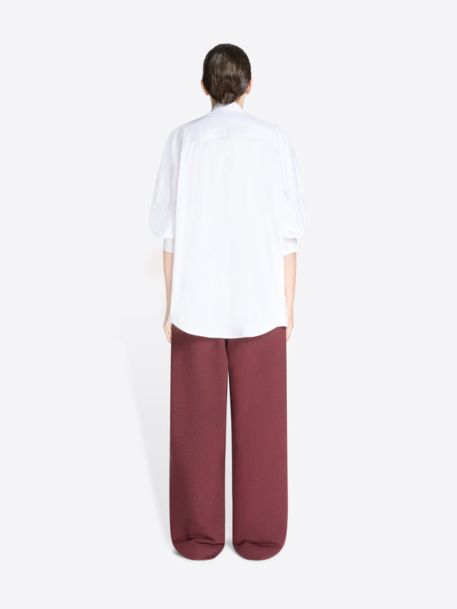 Back view of a person wearing a white shirt and burgundy pants on a white background