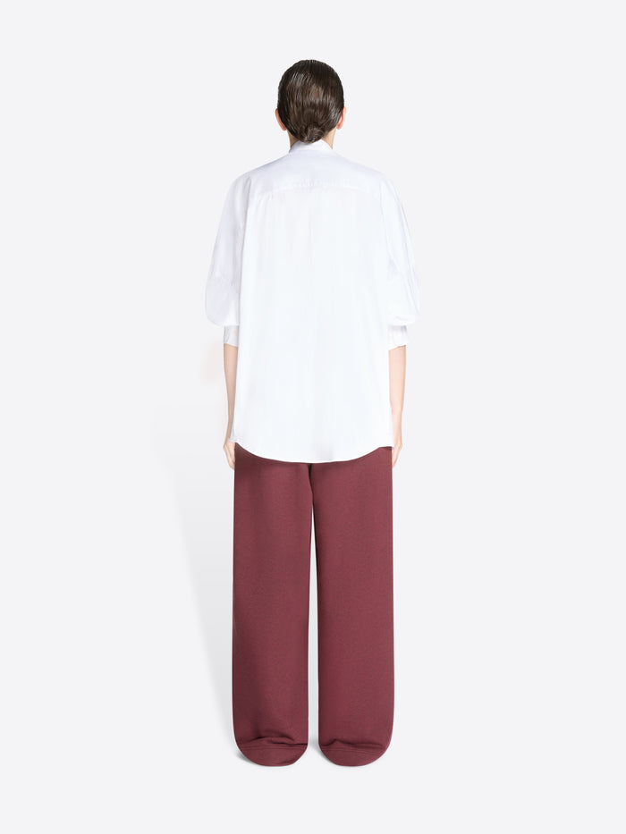 Back view of a person wearing a white shirt and burgundy pants on a white background