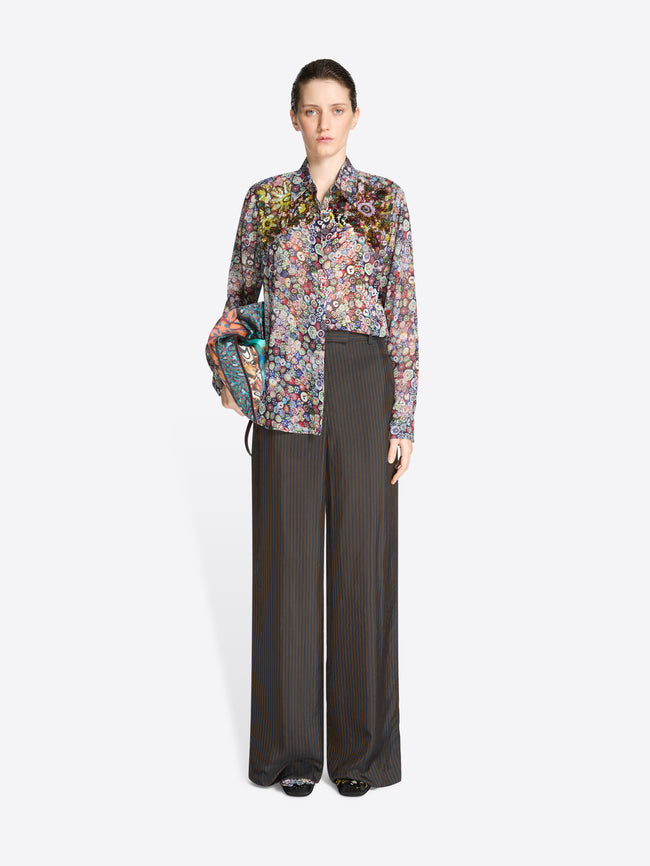 Woman wearing a floral blouse and dark pants holding a bag on a white background
