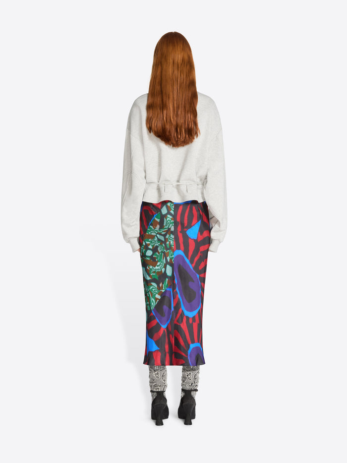 Back view of a person wearing a colorful skirt with abstract patterns and a light-gray sweatshirt on a white background