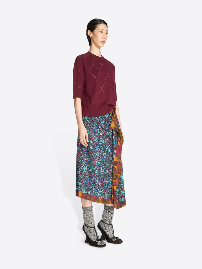 Woman wearing a burgundy knit top and patterned skirt on a white background
