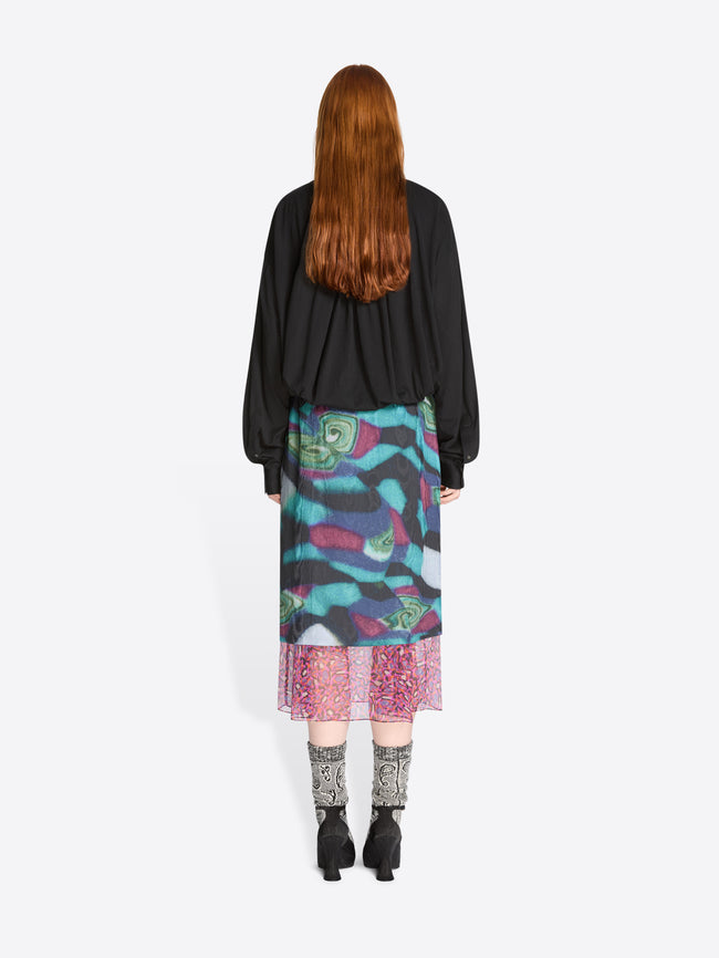 Back view of a person wearing a black shirt and colorful skirt on a white background