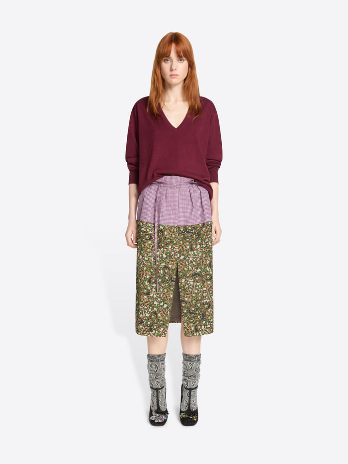 Woman wearing a burgundy sweater and patterned skirt on a white background