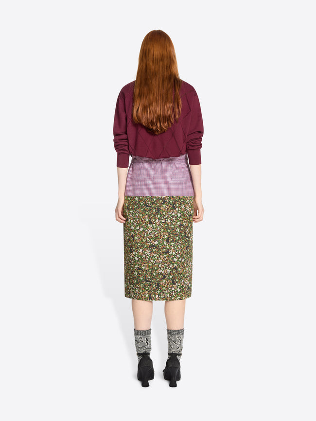 Back view of a person wearing a burgundy sweater and green floral skirt on a white background