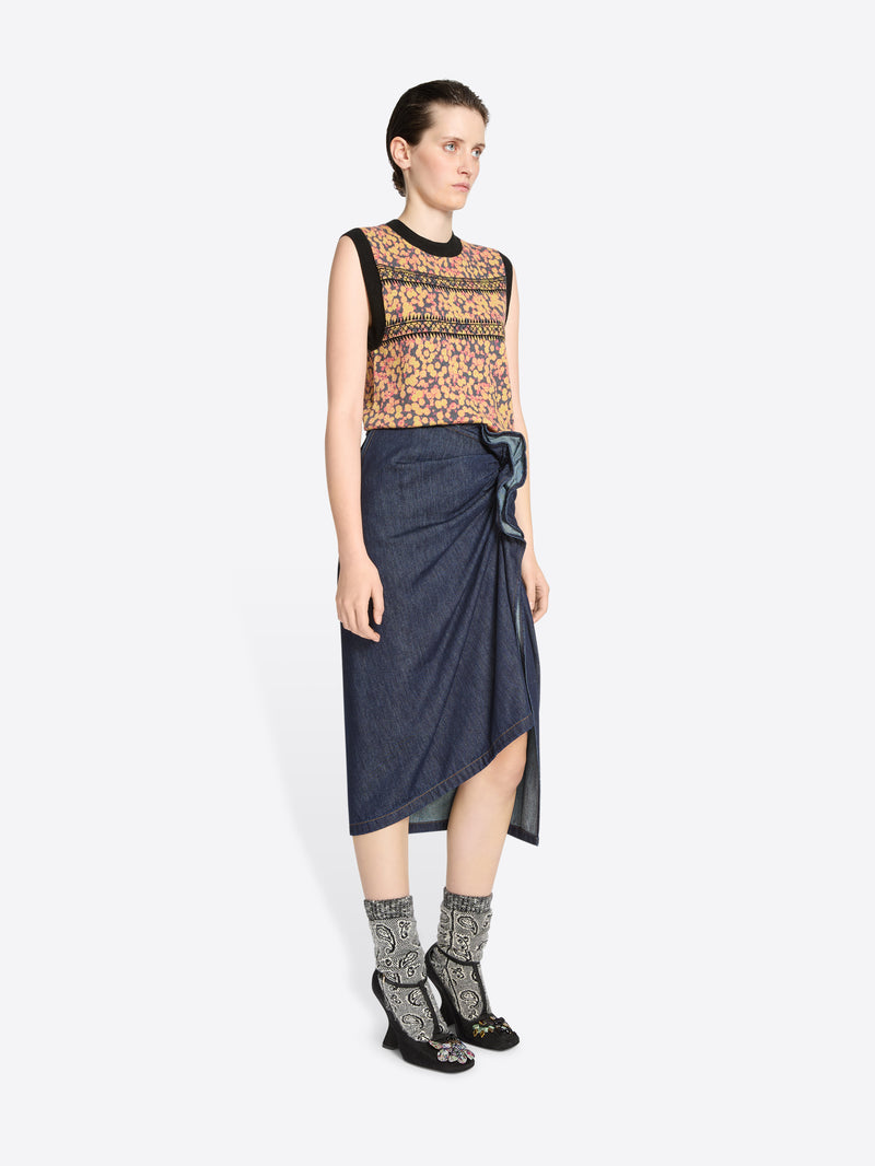 Woman wearing a patterned top and denim skirt on a white background
