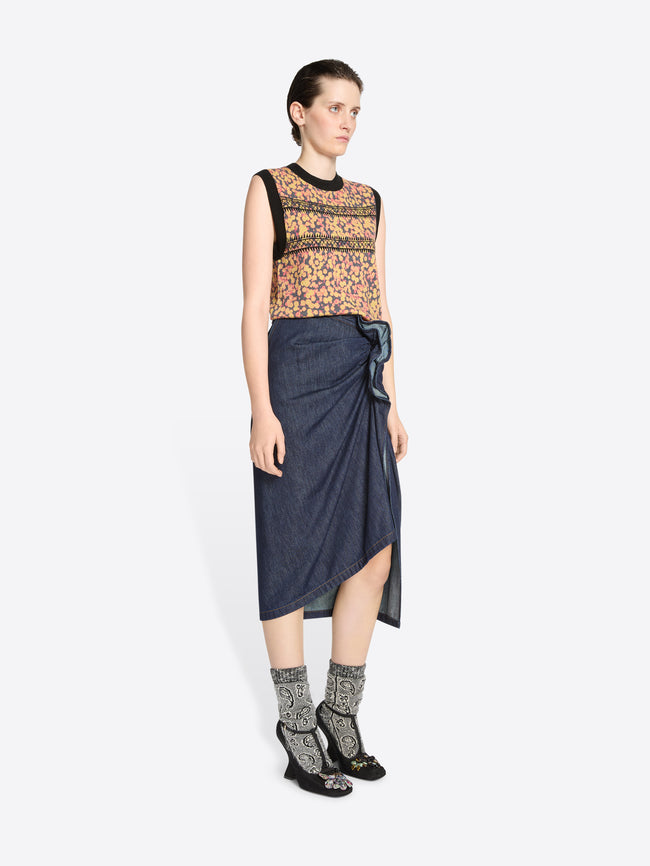 Woman wearing a patterned top and denim skirt on a white background