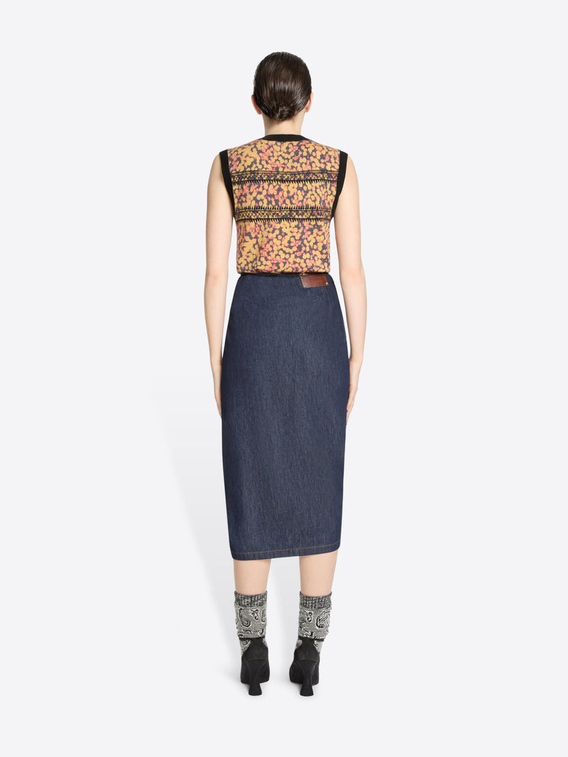 Back view of a woman wearing a sleeveless floral top and denim skirt on a white background