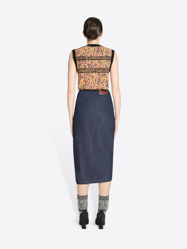 Back view of a woman wearing a sleeveless floral top and denim skirt on a white background