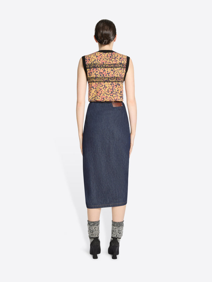 Back view of a woman wearing a sleeveless floral top and denim skirt on a white background