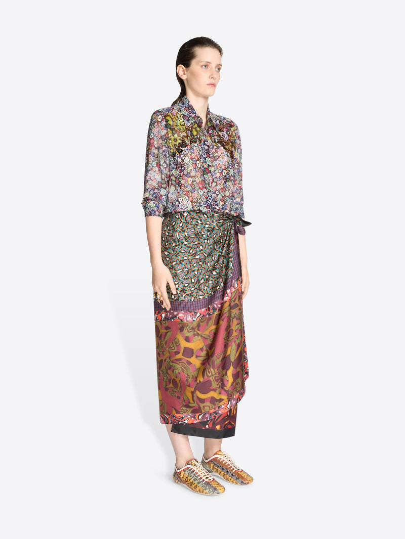 Woman wearing a colorful floral blouse and patterned skirt on a white background